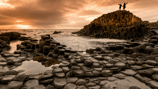 Two visitors standing on top of the Giant's Causeway basalt columns, overlooking the Atlantic